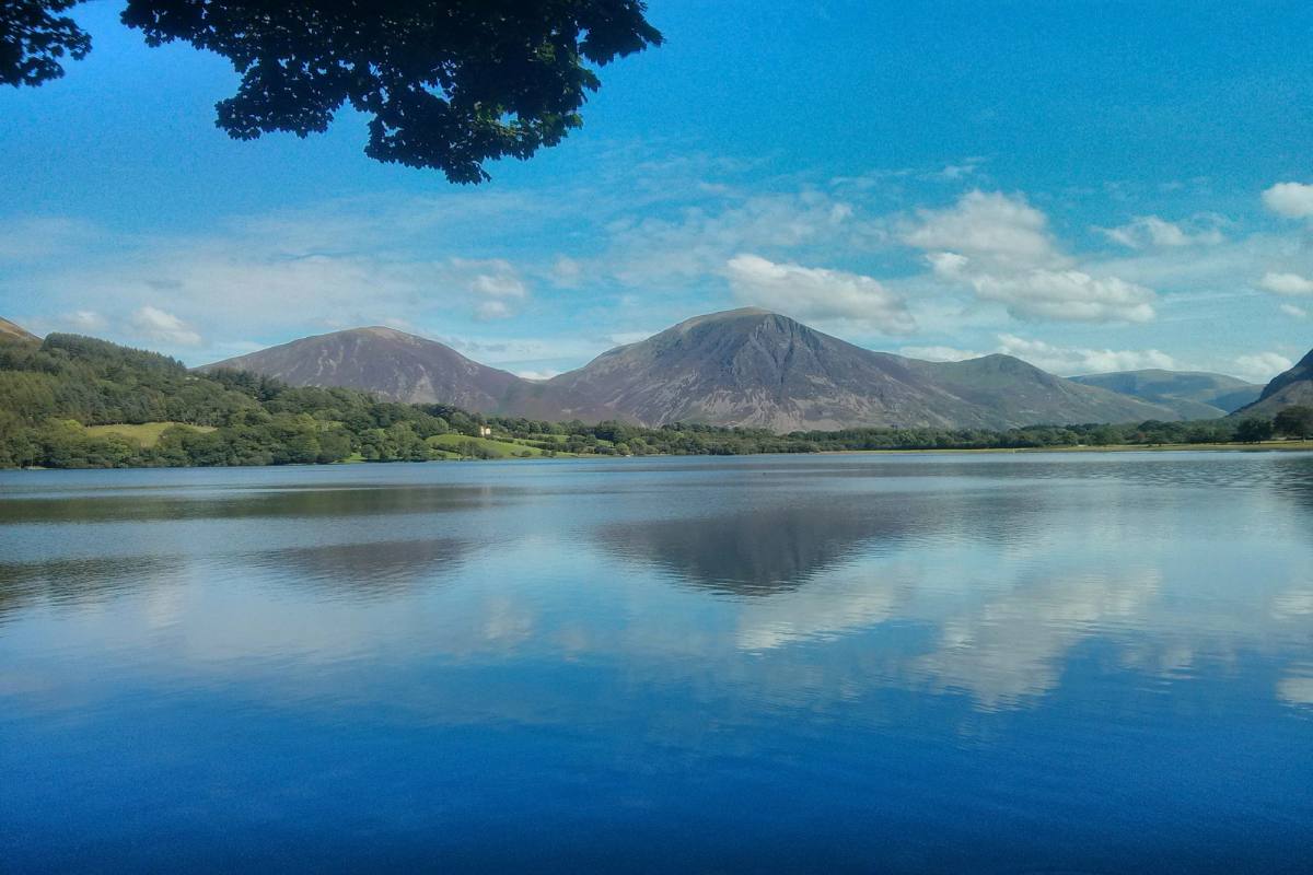 A wide lake lying flat calm with a range of mountains reflected in it
