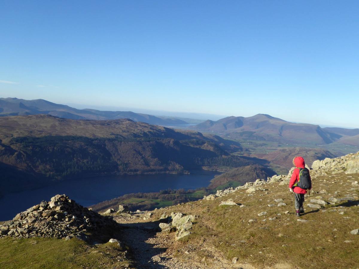 A walker in a red jacket picking along a rocky edge high above Thirlmere