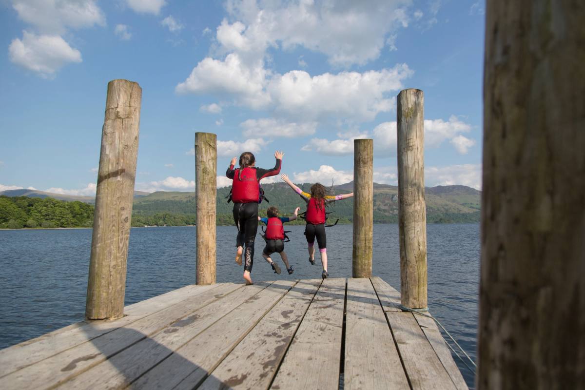 Children leaping from a wooden jetty into the lake, arms in the air
