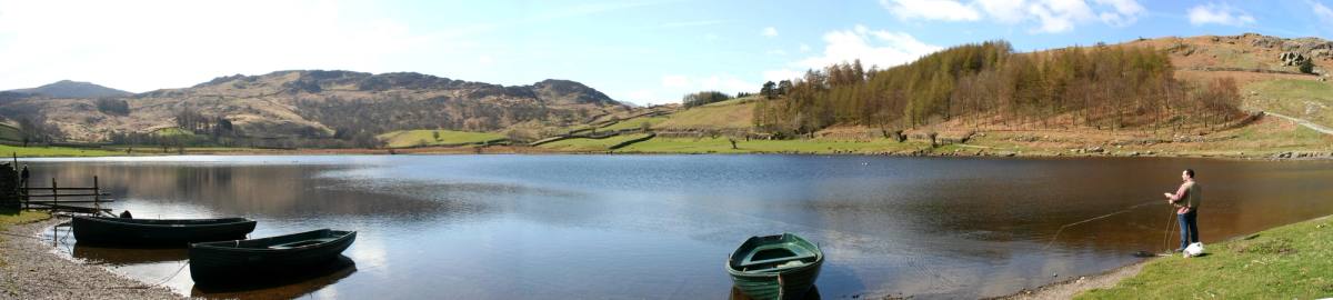 Two rowing boats drawn up on the shore of a tarn with a figure on the far bank