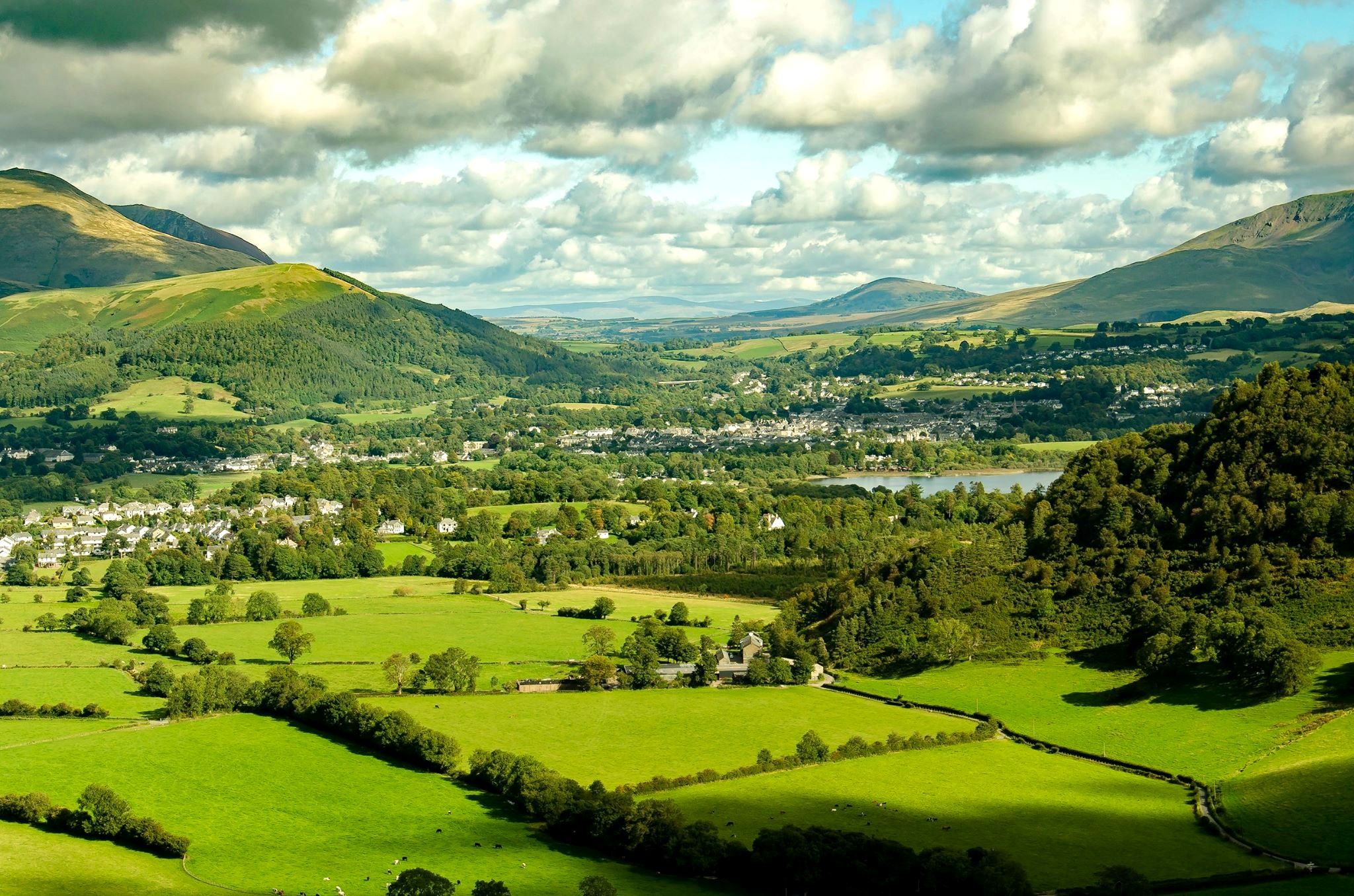 Green fields and hedgerows running out to the fells under towering cloud