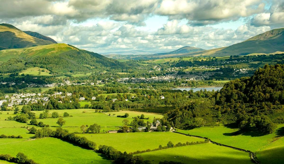 Green fields and hedgerows running out to the fells under towering cloud