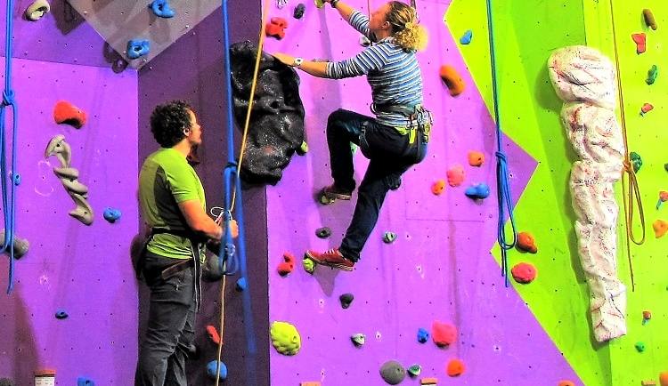 Two climbers working brightly coloured routes on an indoor climbing wall