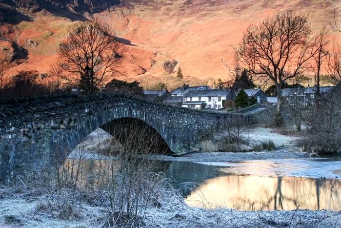 The double arch of Grange bridge over the frozen river with pink light on the crags