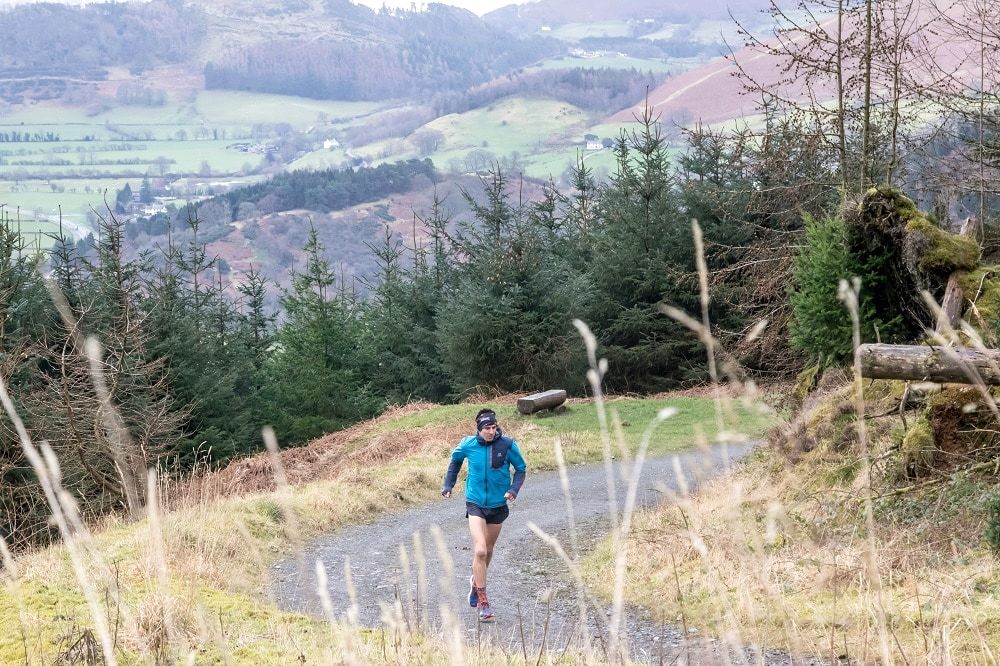 A lone trail runner splashing through a puddle on a forest track
