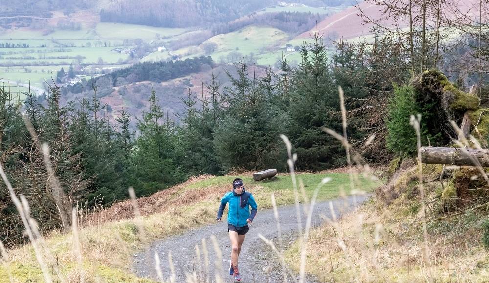 A lone trail runner splashing through a puddle on a forest track