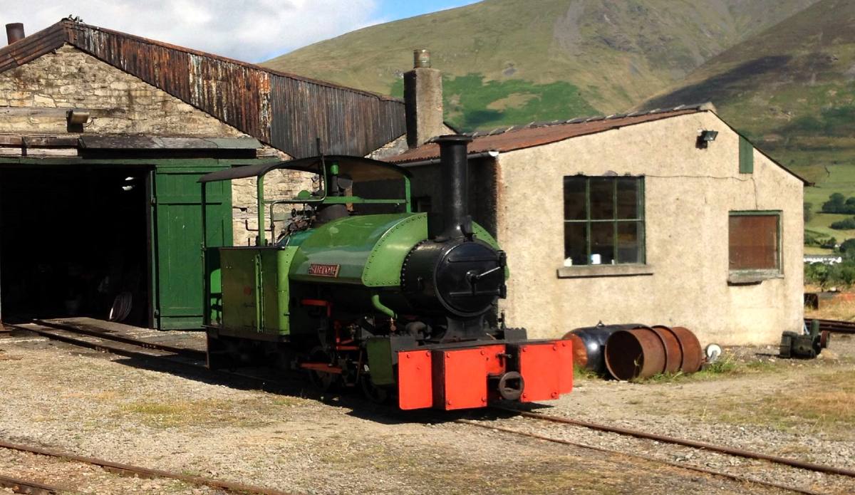 A small green steam locomotive standing outside the engine shed at the quarry museum