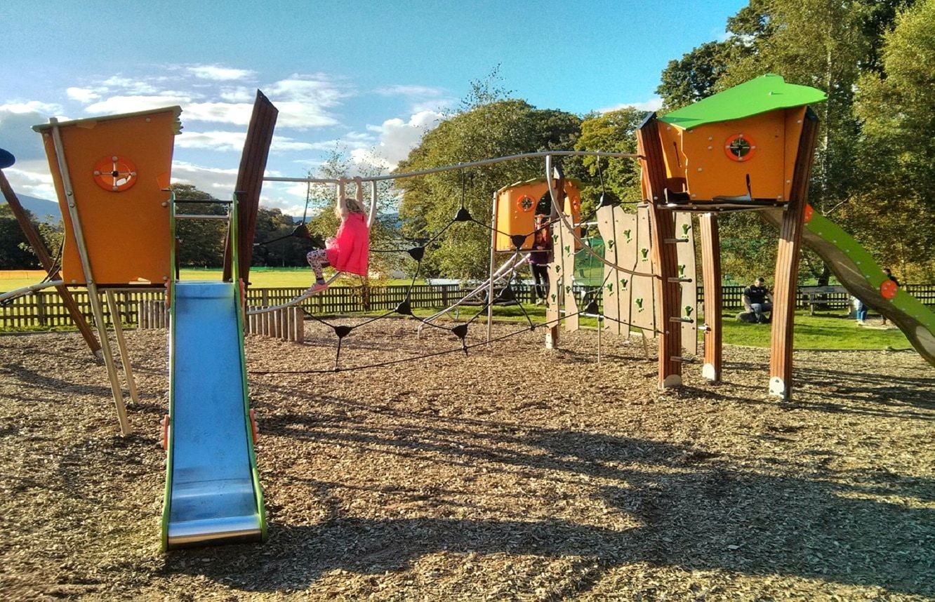 A timber play park with towers and a blue slide on a bark chipping surface