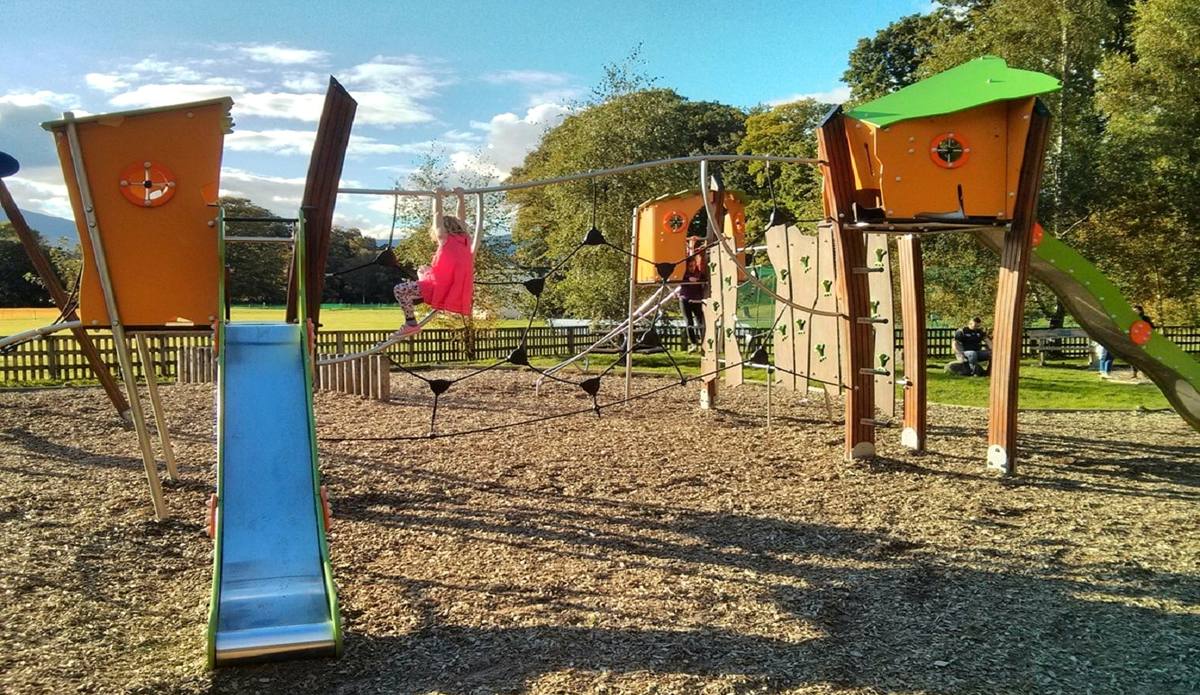 A timber play park with towers and a blue slide on a bark chipping surface
