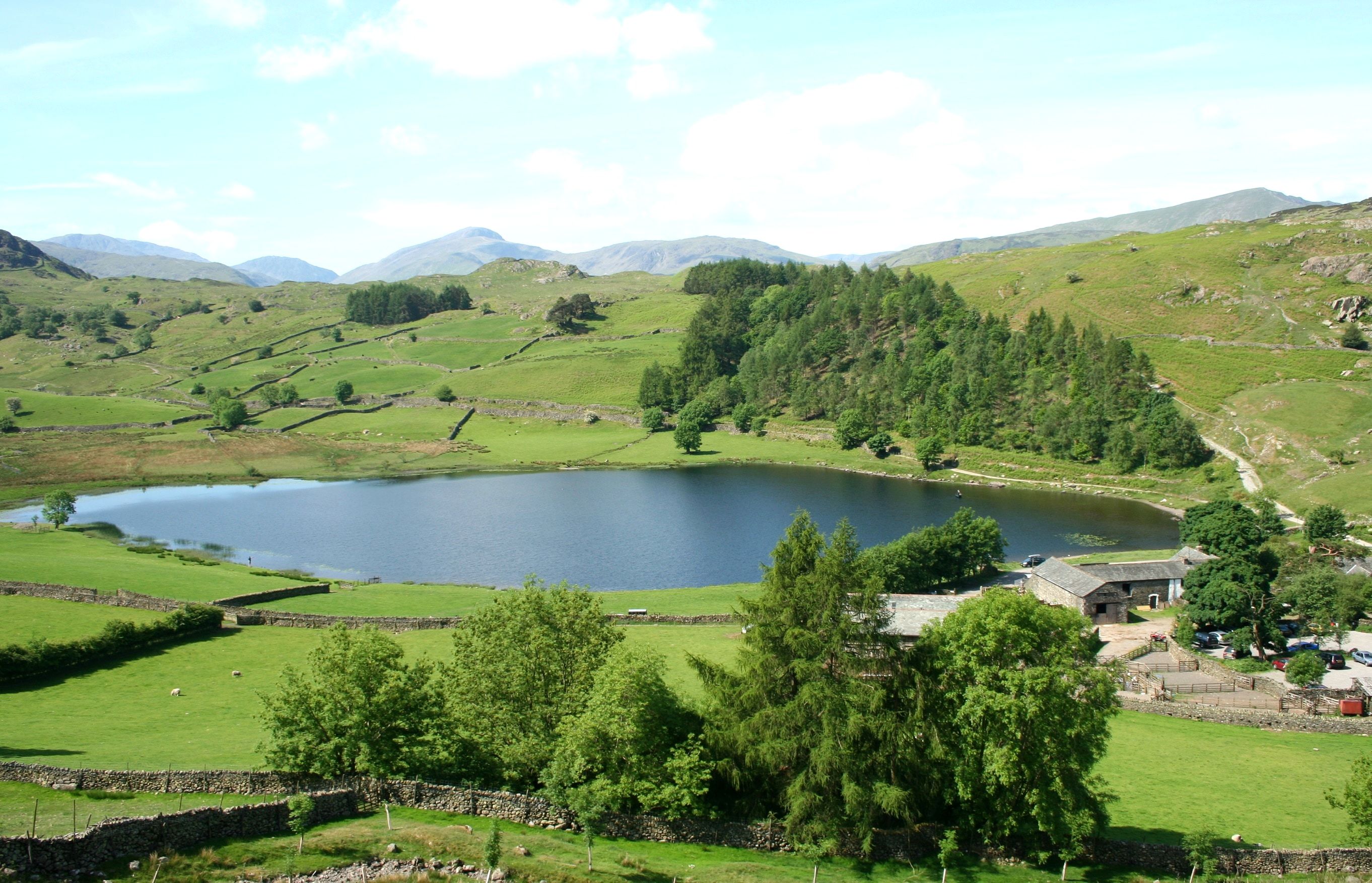 A tarn lying in green hedged fields with the fells rising beyond