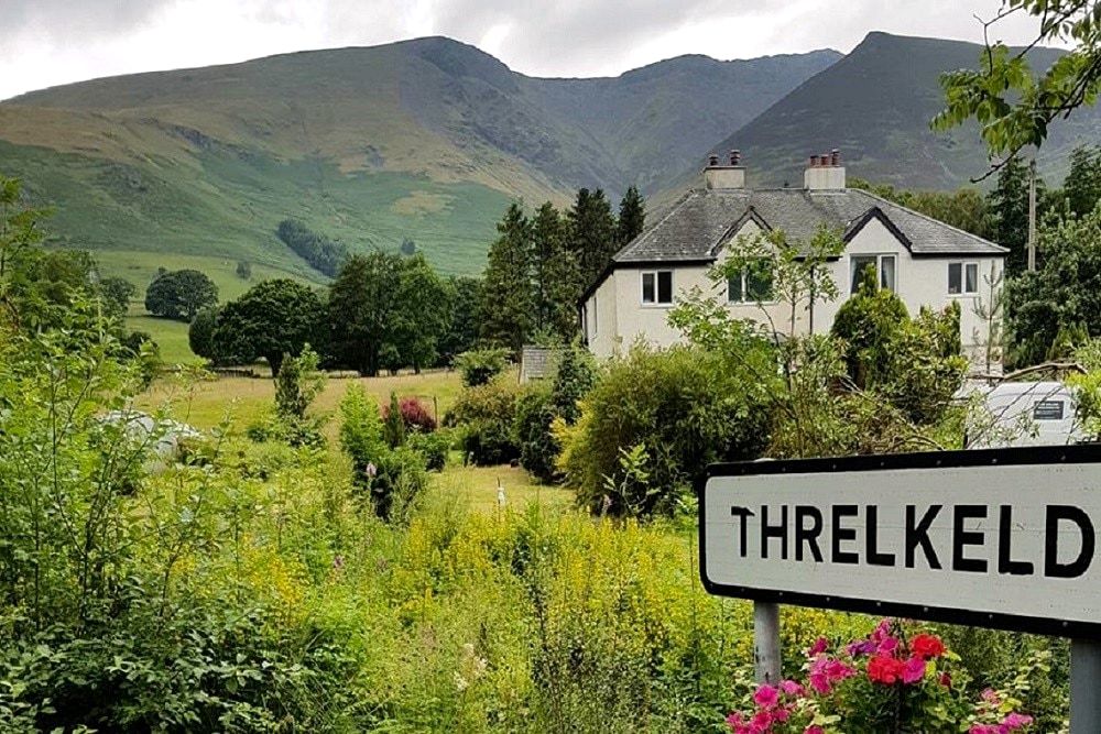 The Threlkeld village sign in front of white houses with Blencathra rising behind