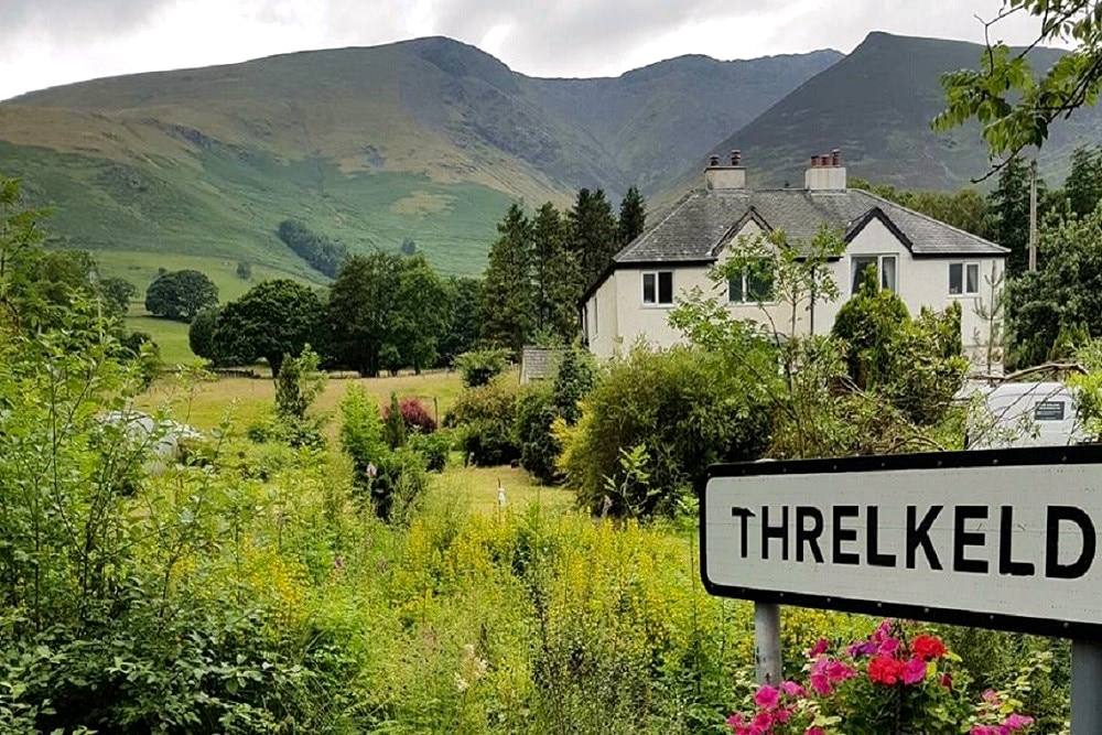 The Threlkeld village sign in front of white houses with Blencathra rising behind