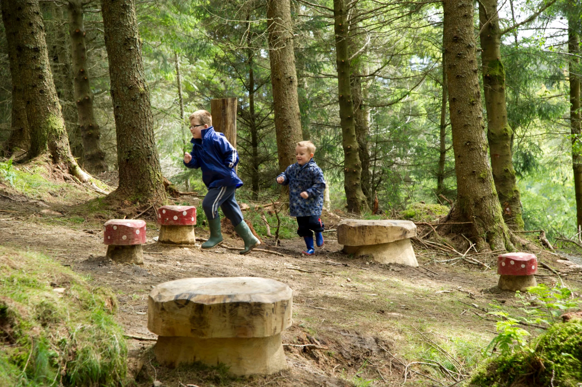 Two children playing among carved stone stools in a forest clearing