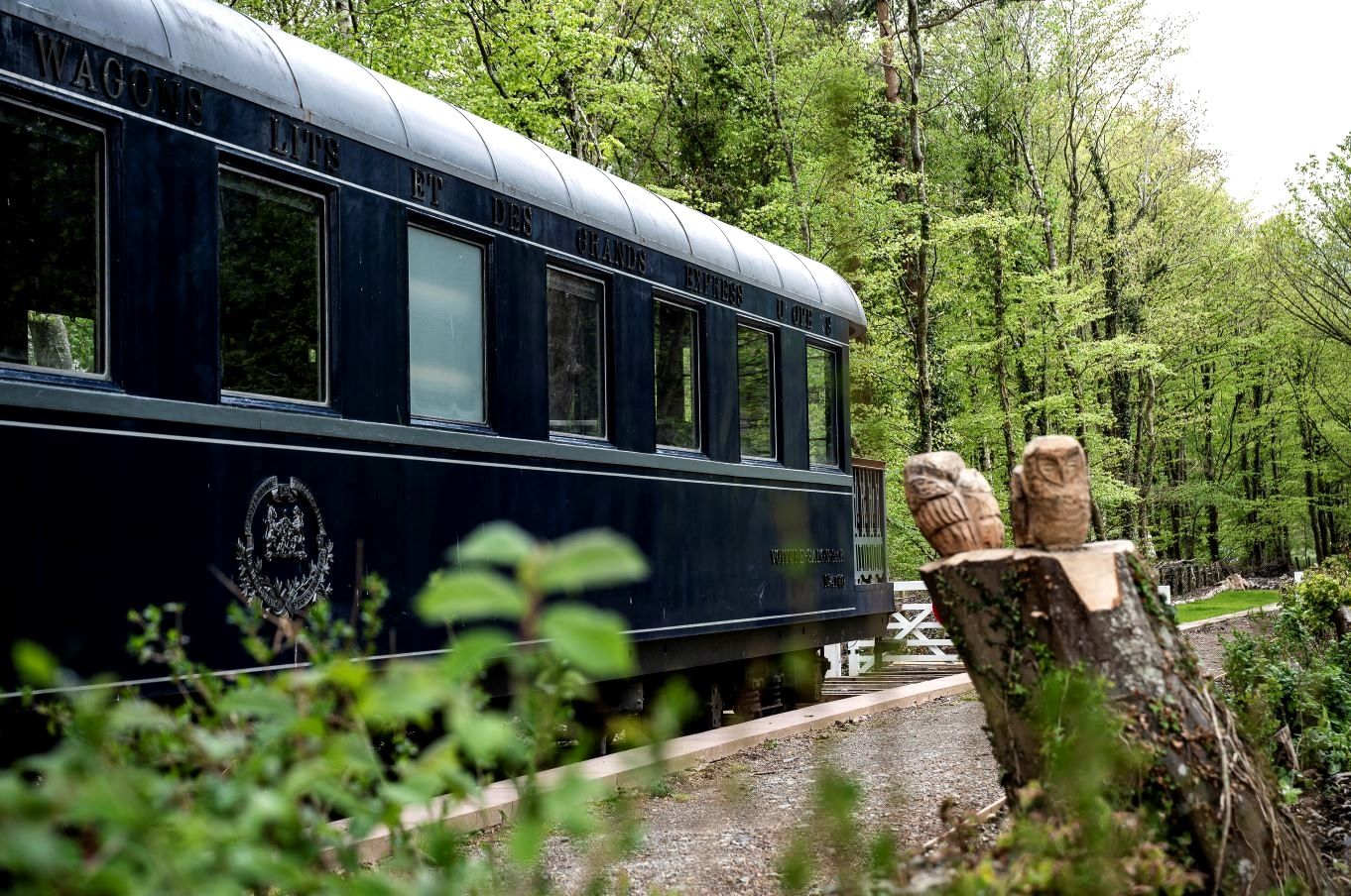A restored dark blue Pullman railway carriage standing among trees at the old station