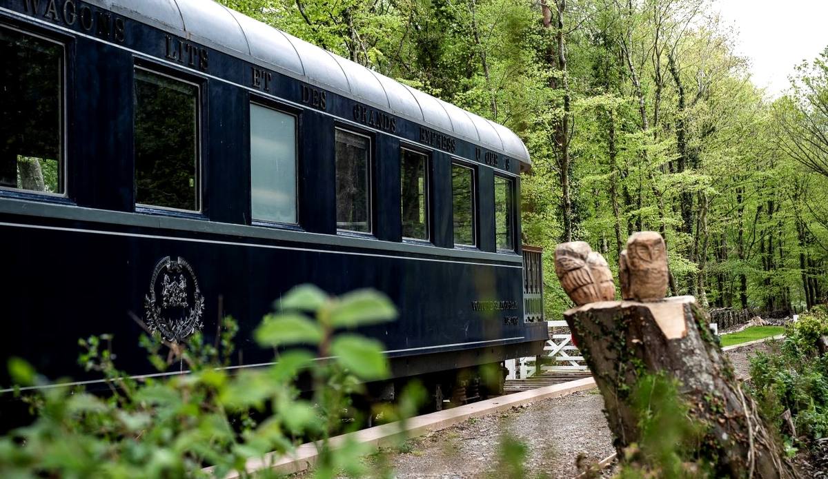 A restored dark blue Pullman railway carriage standing among trees at the old station