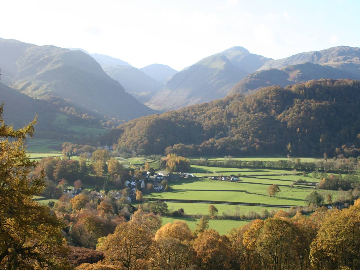 autumn view of rosthwaite, green fields, brown/orange trees and mountains in the background 