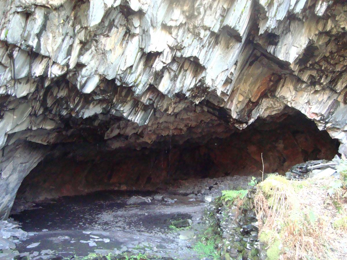 The dark rust-streaked mouth of the cave cut into the quarried rock