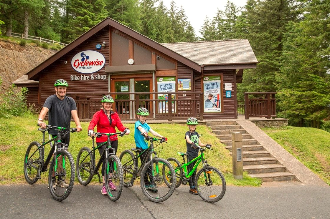 A family of four on mountain bikes outside a timber bike hire and shop building