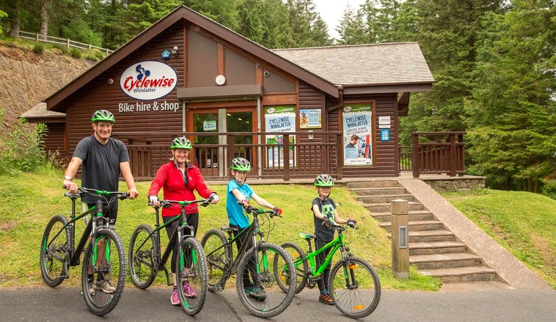 A family of four on mountain bikes outside a timber bike hire and shop building