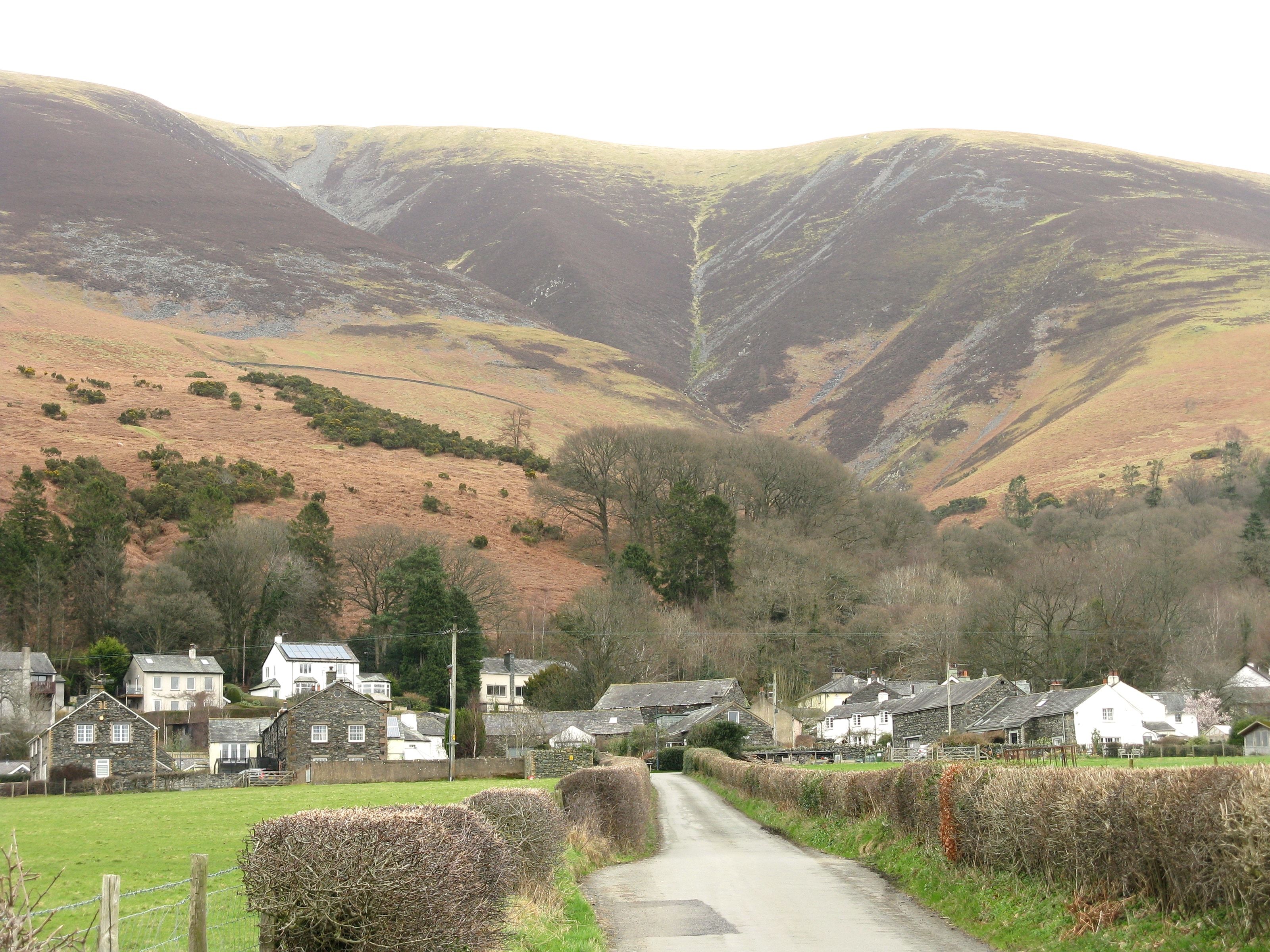 A lane running between village cottages with the long flank of Skiddaw rising above