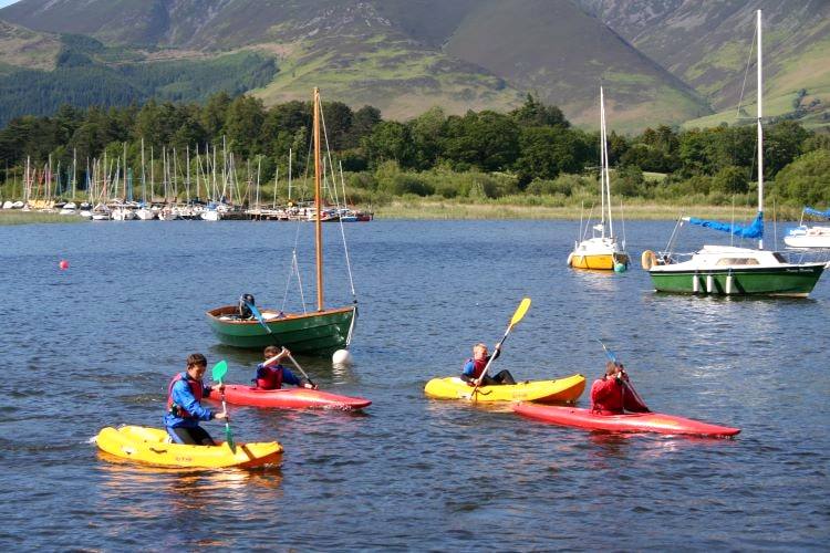Kayakers in bright boats paddling among moored sailing dinghies