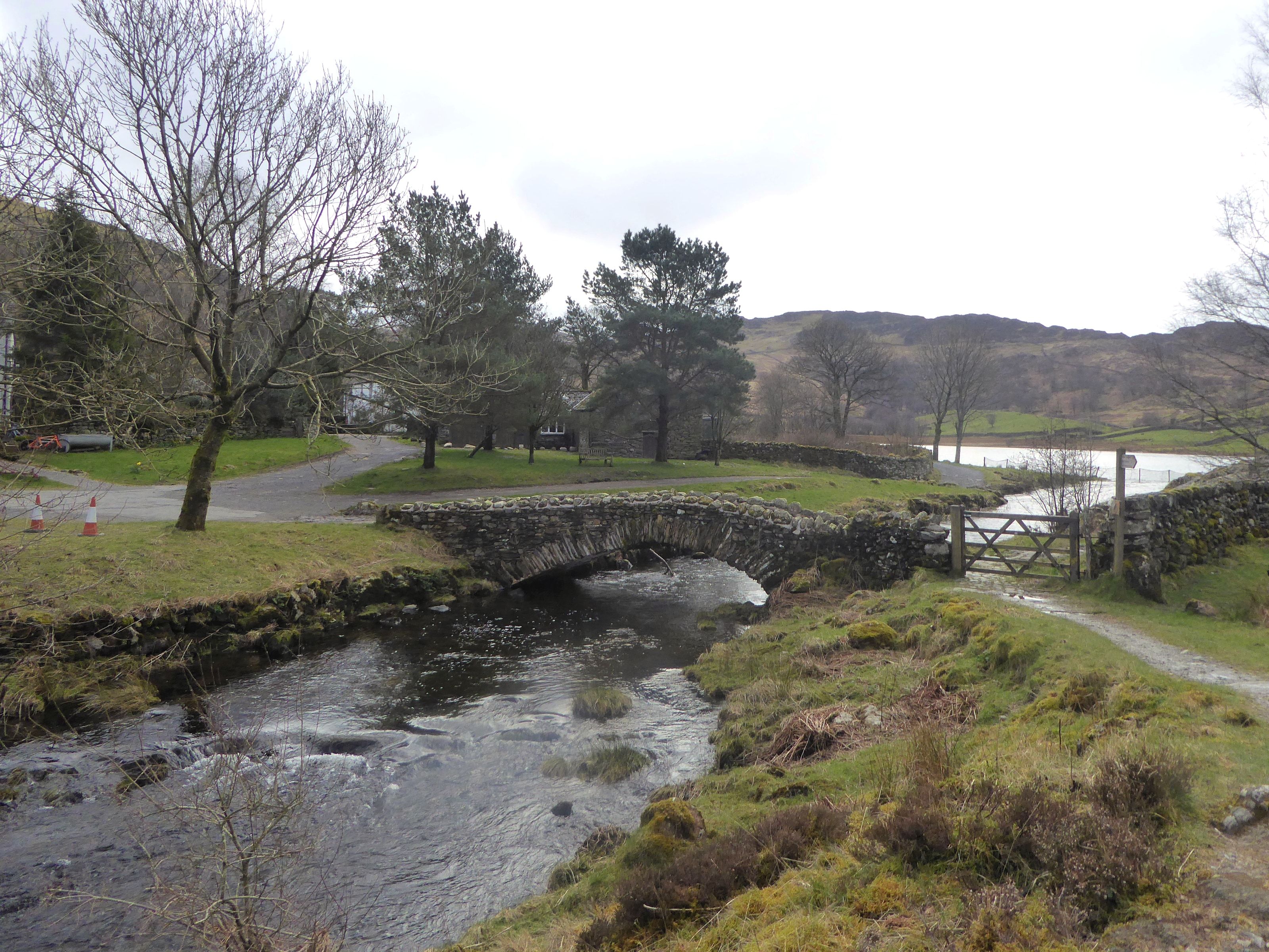 A stone packhorse bridge over a wide shallow beck beside a drystone wall