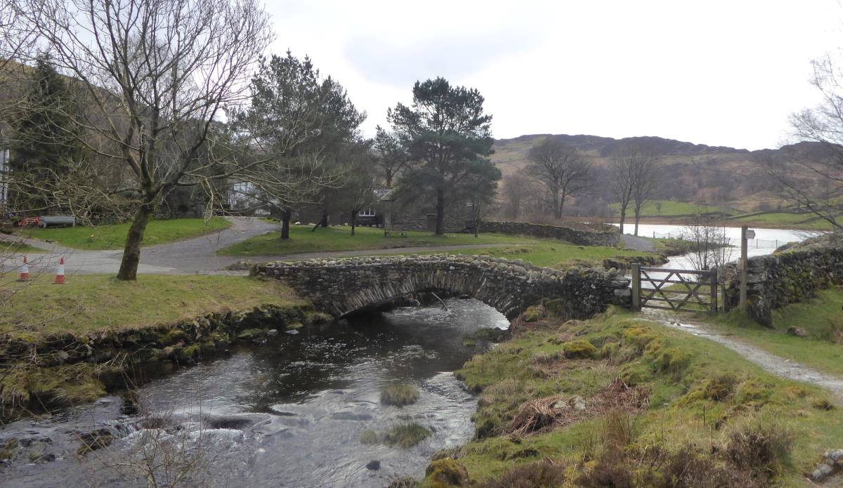 A stone packhorse bridge over a wide shallow beck beside a drystone wall