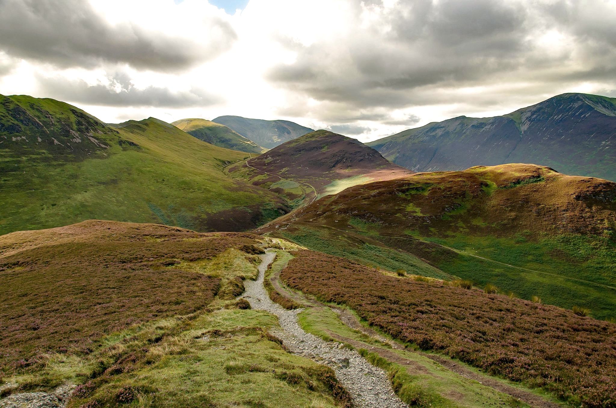 A stony path winding into a bracken-covered valley between steep fells