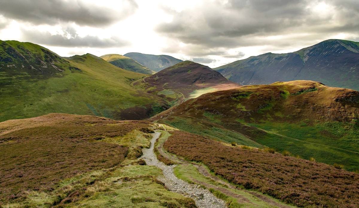 A stony path winding into a bracken-covered valley between steep fells