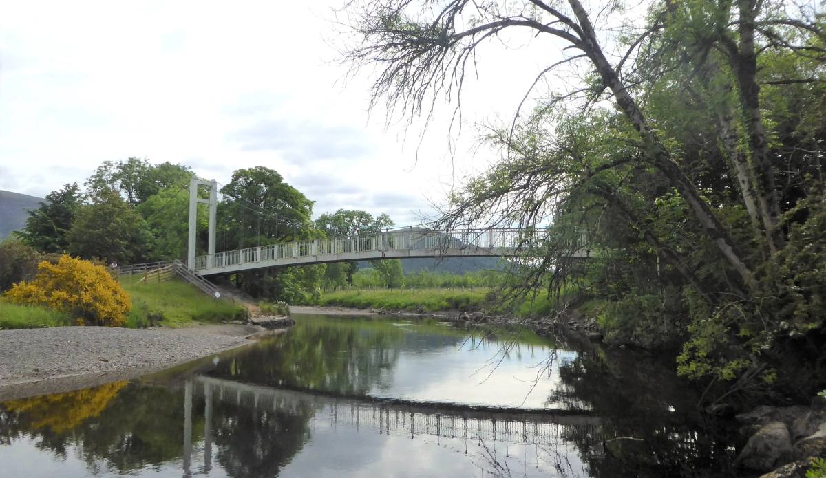 A white suspension footbridge crossing the river Derwent between wooded banks
