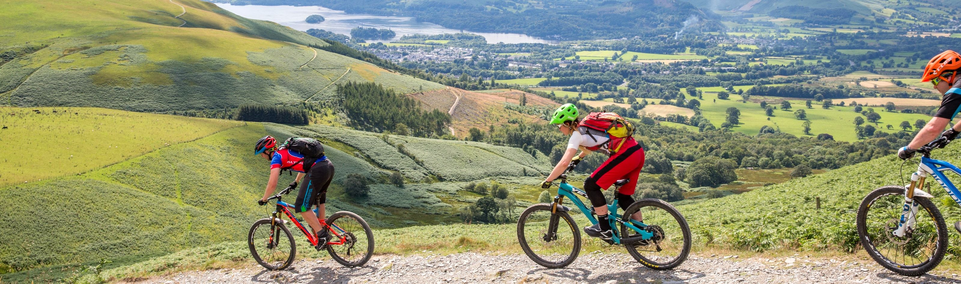 Three mountain bikers riding a stony track with the whole valley spread out below