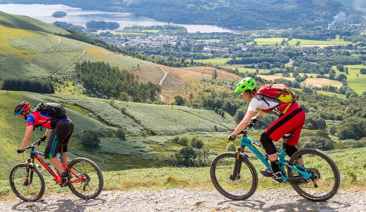 Three mountain bikers riding a stony track with the whole valley spread out below