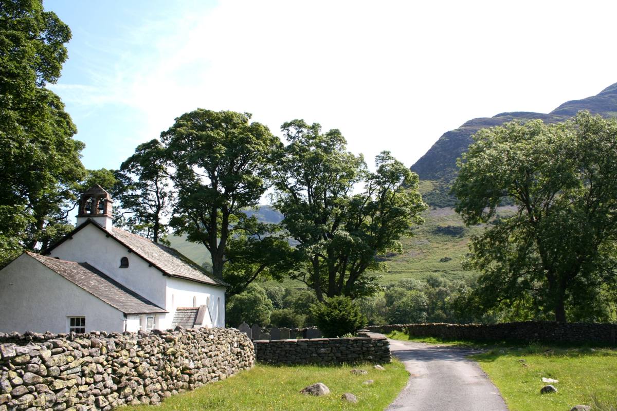 A whitewashed cottage beside a walled country lane with fells rising behind