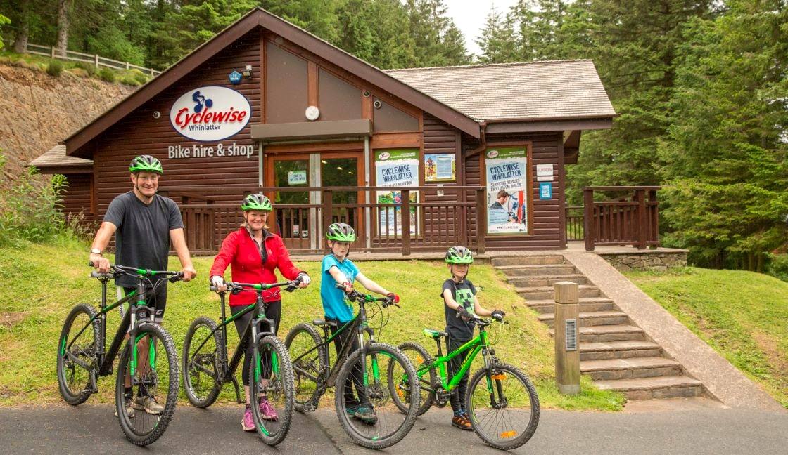 A family of four standing with mountain bikes outside the timber bike hire building