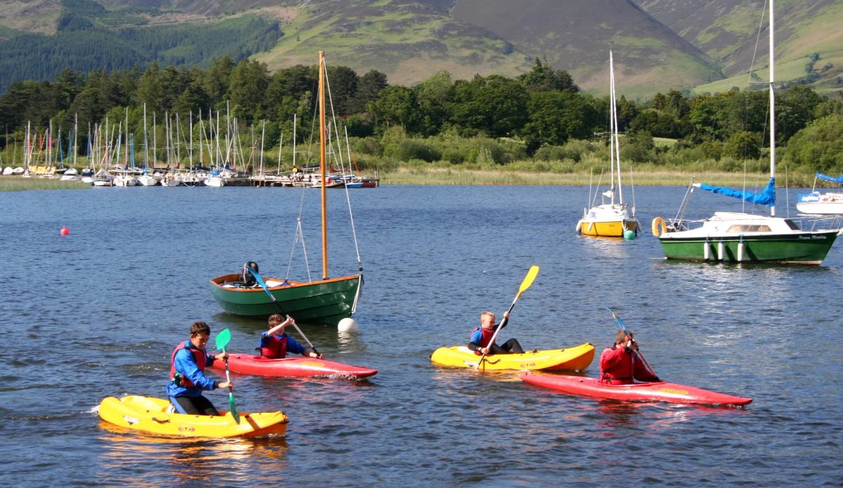 Kayakers paddling past moored sailing dinghies on a lake