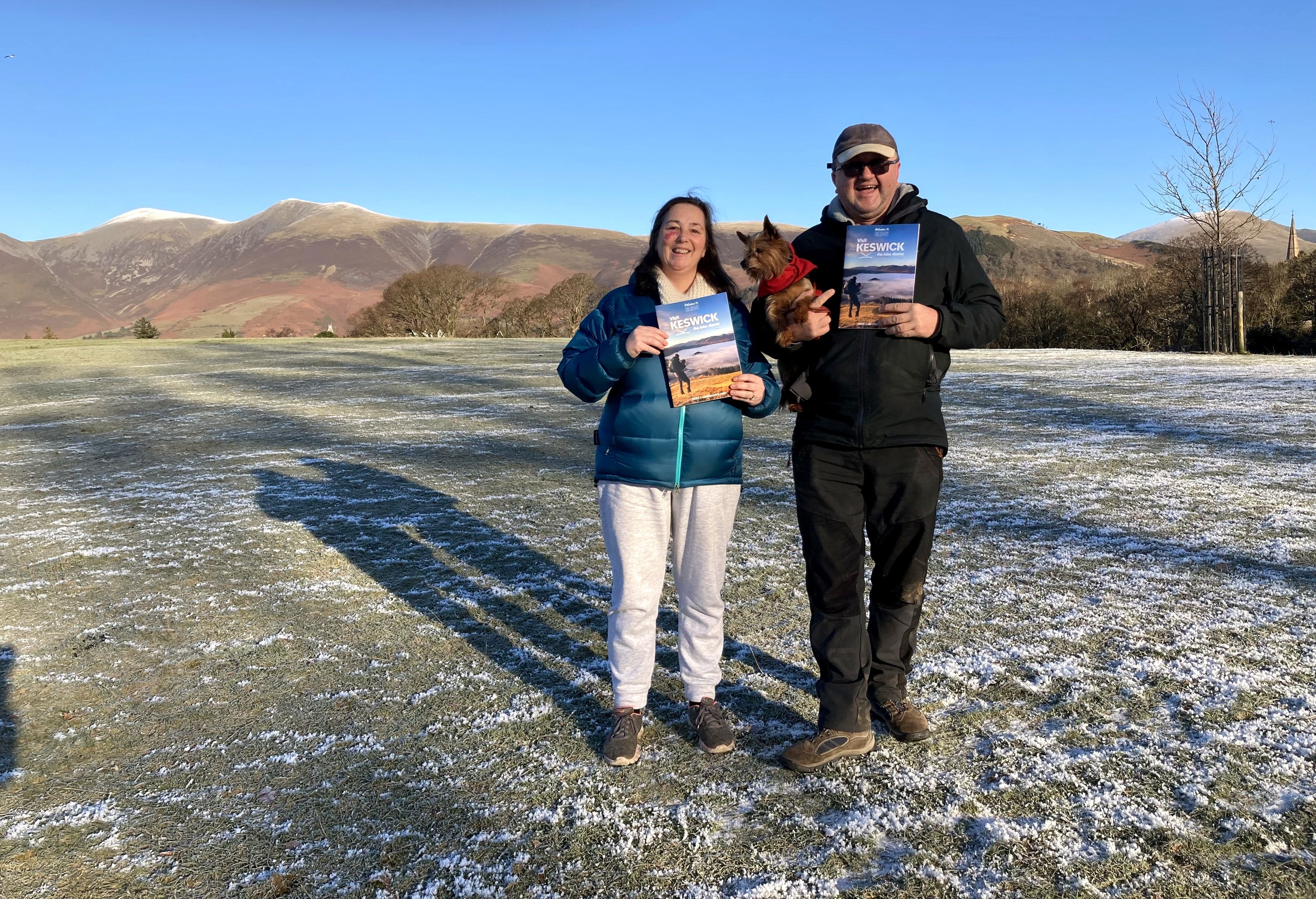 Two people holding copies of the Visit Keswick Guide in Crow Park