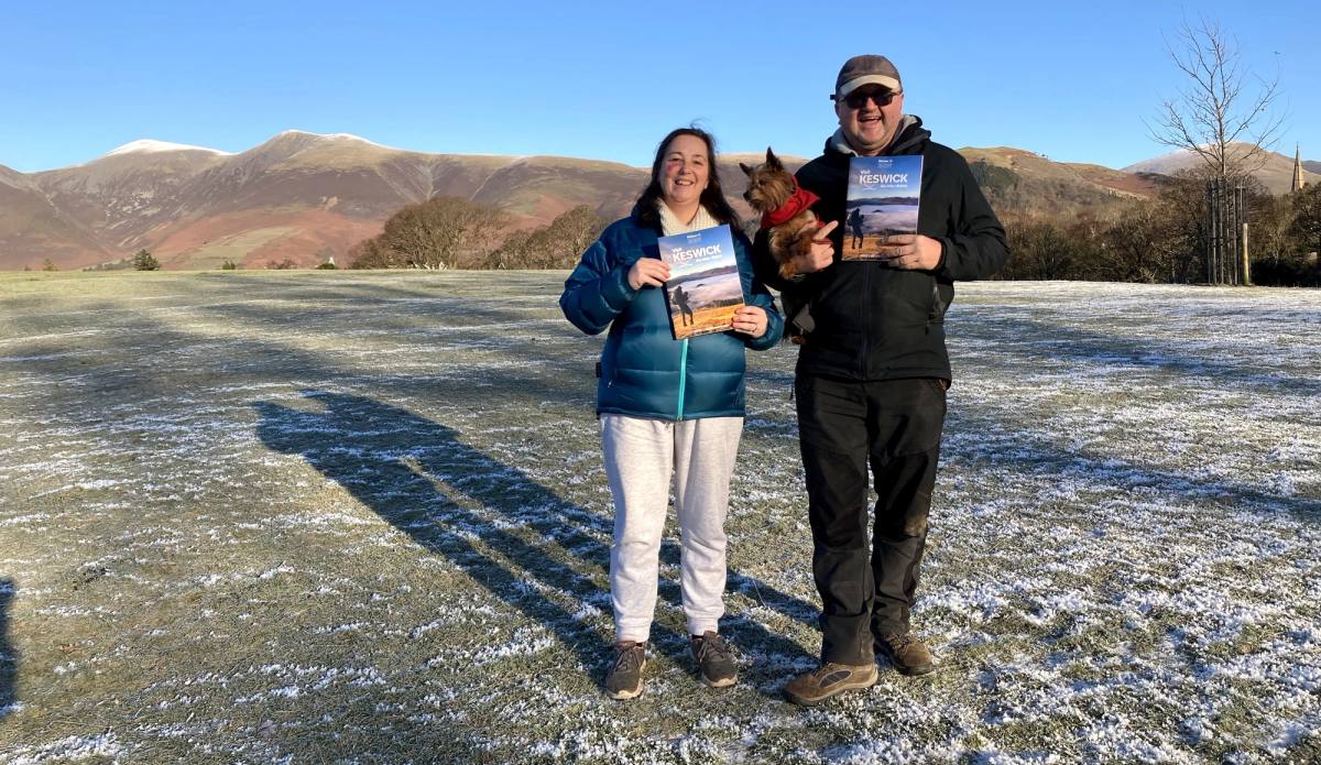Two people holding copies of the Visit Keswick Guide in Crow Park