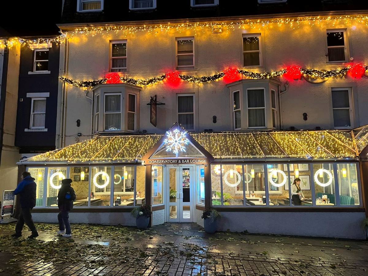 The Moot Hall hung with lit Christmas garlands with people passing below