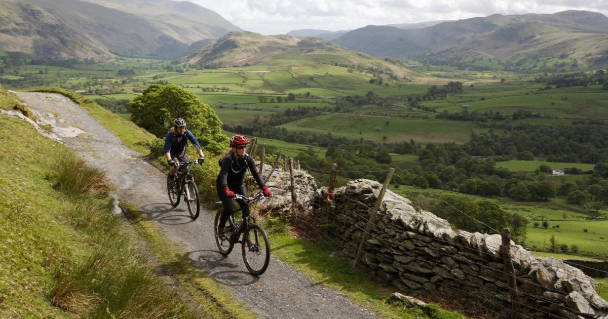 Two cyclists riding side by side along the smooth railway path between fields