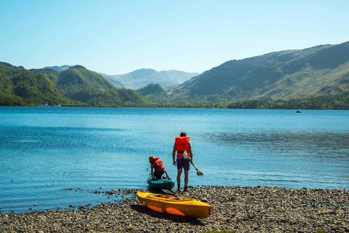 A paddler beside a yellow kayak on the shingle shore, fells across the water