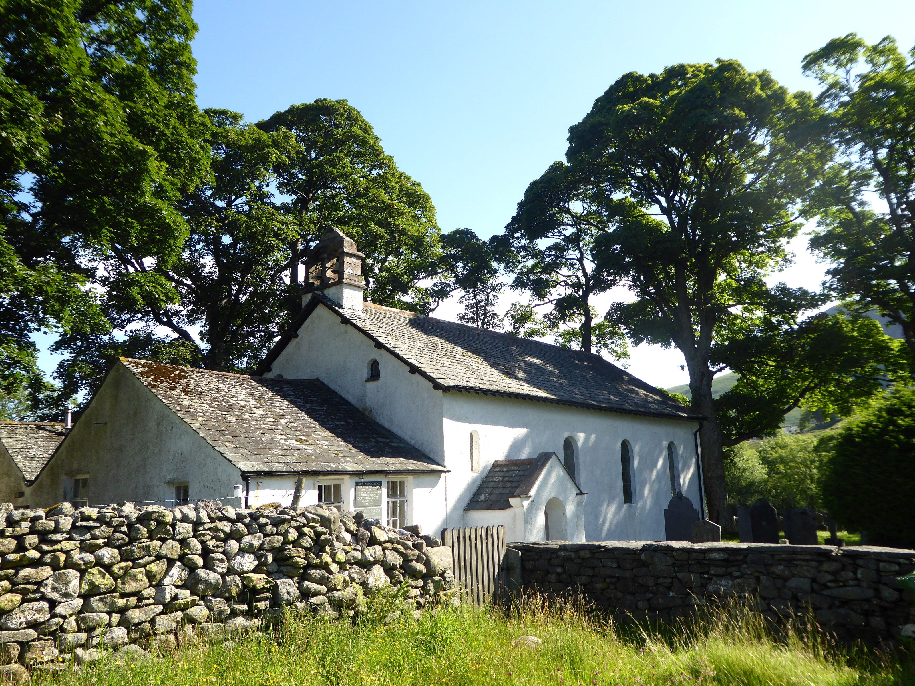 The small whitewashed Newlands church behind a drystone wall under a large tree