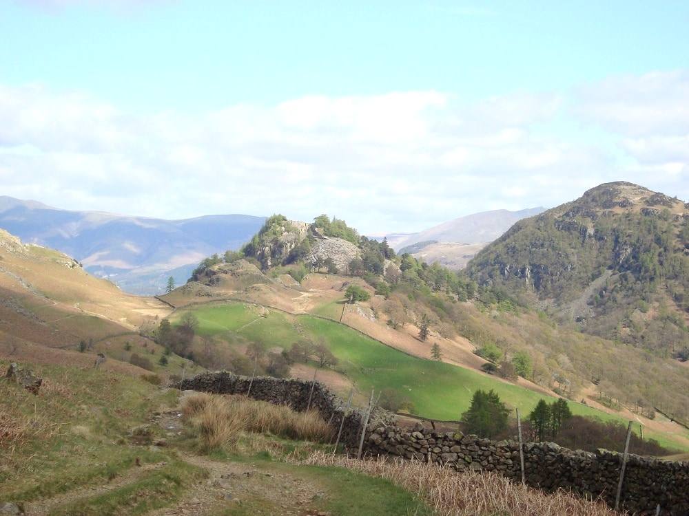 The wooded cone of Castle Crag rising above walled fields in the valley