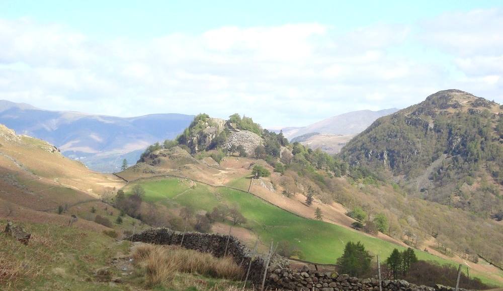 The wooded cone of Castle Crag rising above walled fields in the valley