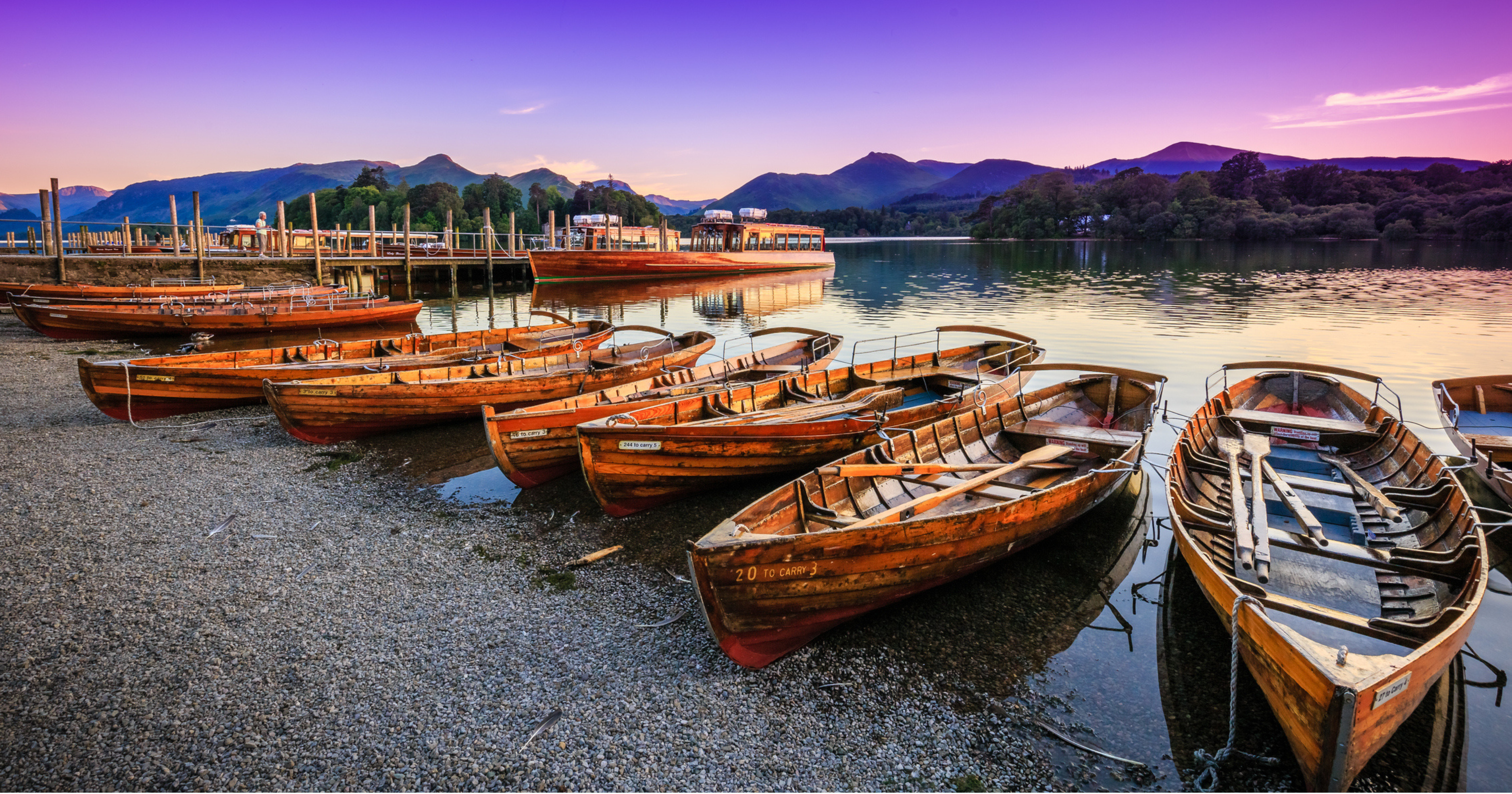 Wooden boats on the shores of Derwentwater with a sunrise sky