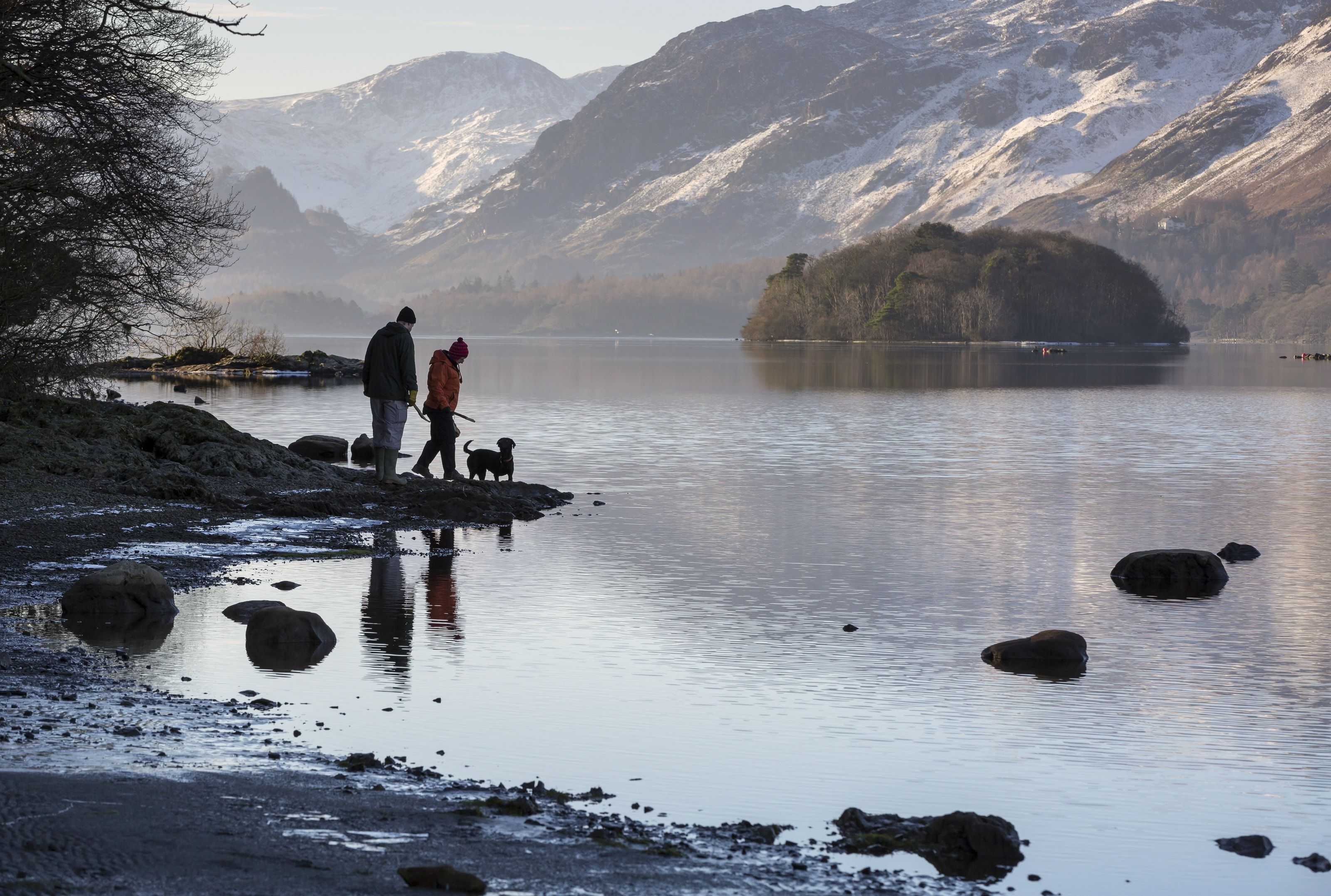 Couple with dog walking on the shores of Derwentwater in winter