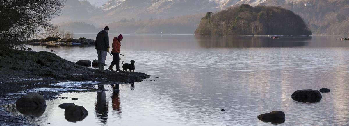 Couple with dog walking on the shores of Derwentwater in winter