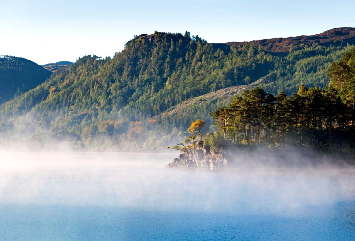 A wooded crag at the edge of Thirlmere with mist lying across the water