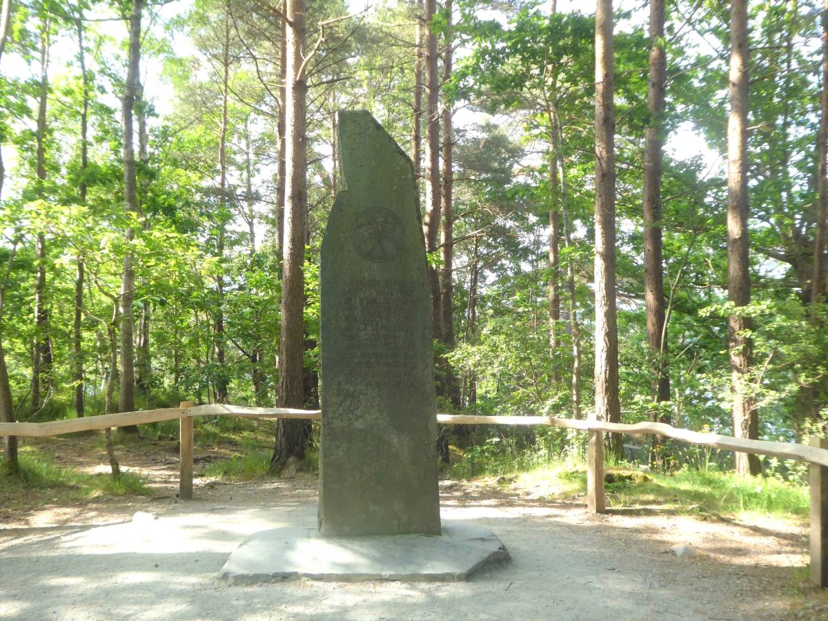 The standing stone of the Ruskin memorial in a railed clearing among tall pines