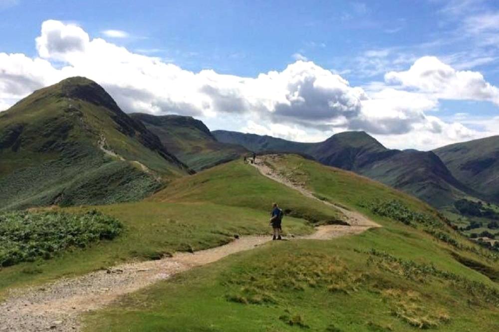 Walkers on the grassy ridge path with fells rolling away on both sides