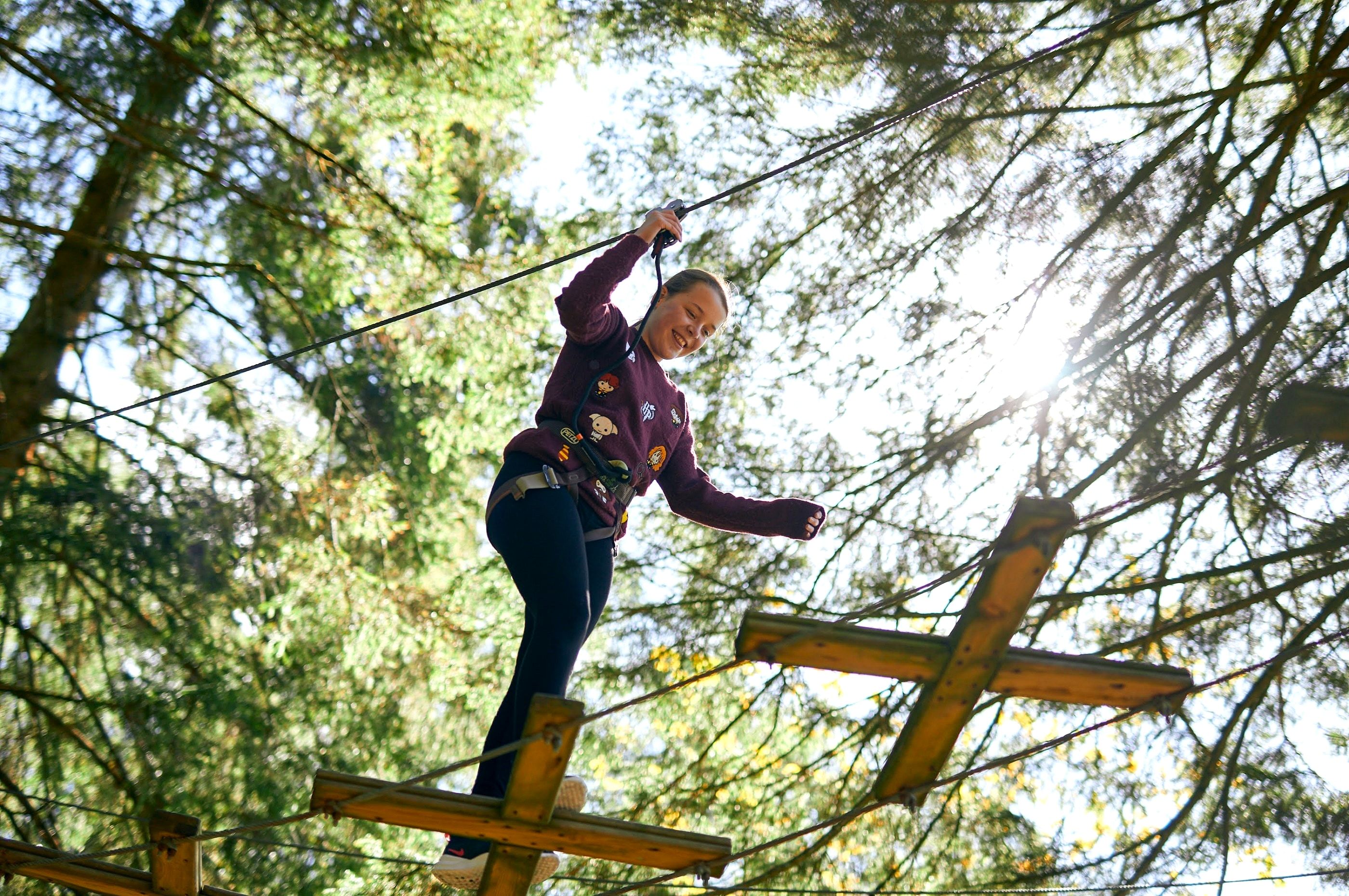 A person balancing along a high rope bridge in the tree canopy of an adventure course
